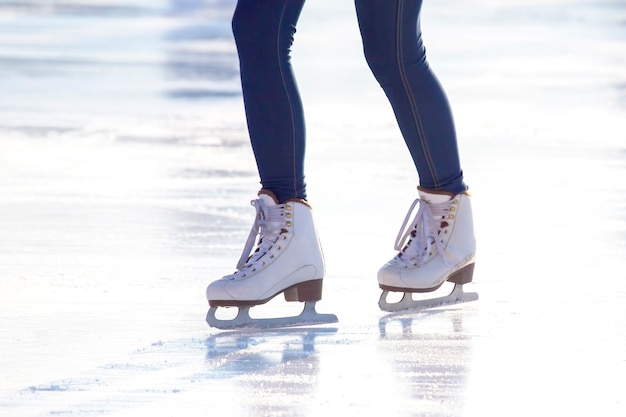 Photo legs of a girl in blue jeans and white skates on an ice rink. hobbies and leisure. winter sports