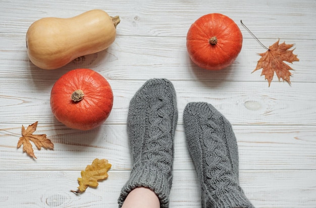 Legs of a girl in knitted socks on a wooden background next to pumpkins and autumn leaves