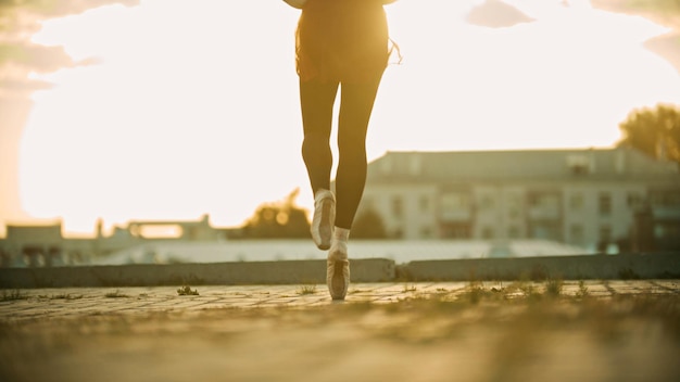 彼女のつま先の夕日の屋根の上を走っている優雅な若い女性のバレリーナの足