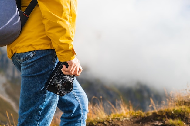 Legs of hiking woman standing and holding a camera on peak of mountain covered by clouds