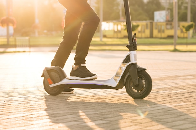 Legs hipster in black sneakers riding an electric scooter road to work the modern way. Fast speed driving electric transport. E-scooter rider, man ride sharing or rent personal eco transportation