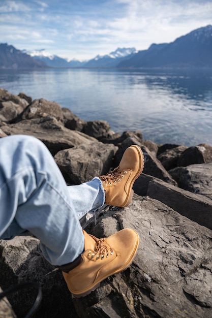 Legs in jeans and hiking boots on the rocks near mountain lake with water reflection