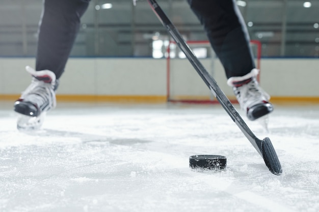 Photo legs of male hockey player in sports uniform and skates moving down rink in front of camera against stadium environment while going to shoot puck