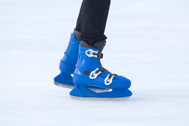 파란색 스케이트를 입은 남자의 다리가 아이스링크를 타고 있습니다. 취미와 스포츠. 휴가 및 겨울 활동.
