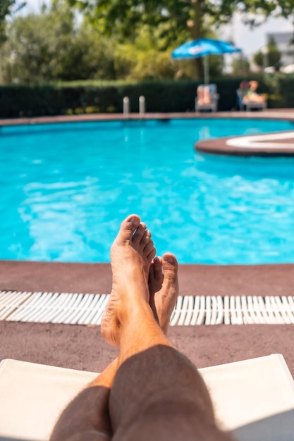 The legs of a man relaxing on a deck chair overlooking the water sunbathing by the pool