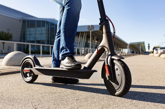 Legs of a man standing on e-scooter parked on sidewalk