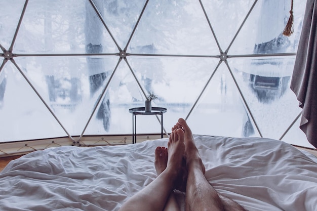 Legs of a man and woman couple in bed against the background of a snowcovered forest in a dome camping