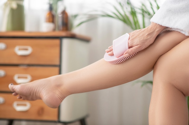 Legs massage. Woman in white massaging her legs with massaging device