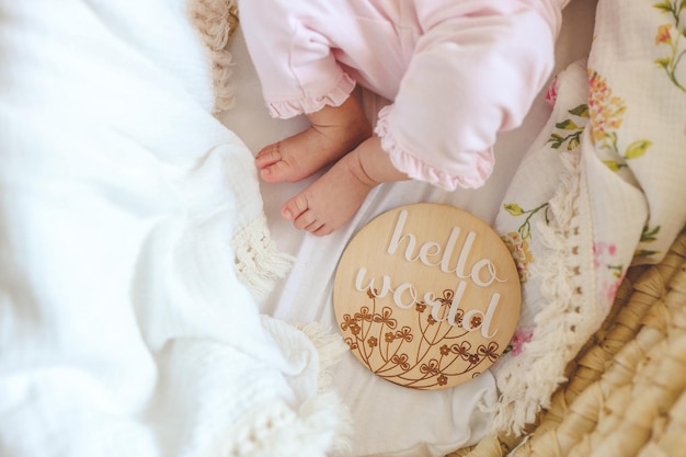 Photo legs of a newborn baby and a wooden board with the inscription hello world