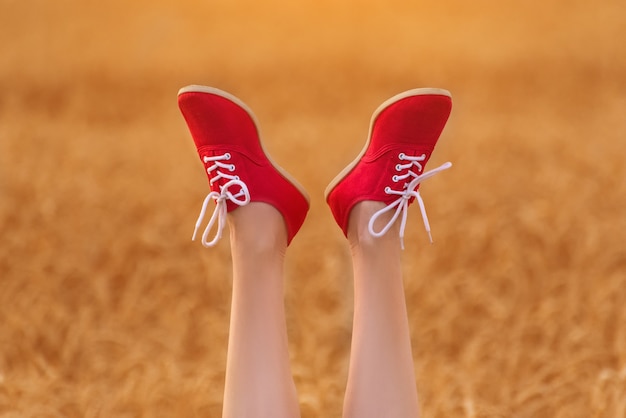 Legs in red shoes raised upwards. Woman on wheat field.