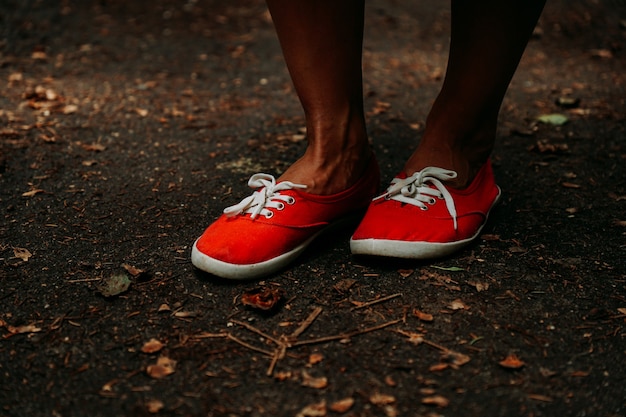 Legs in red sneakers on an autumn path in the park. Black leather legs. Sport in summer forest