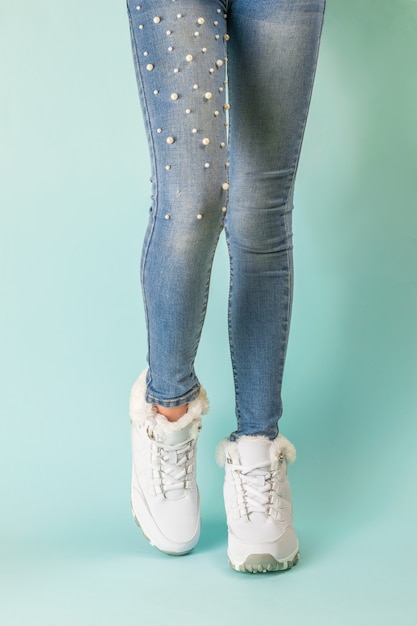 Legs of a slender girl in tight jeans and white warm sneakers. Winter sports style.