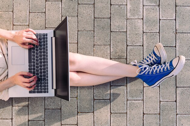 Legs of a teenage woman in sneakers with a computer