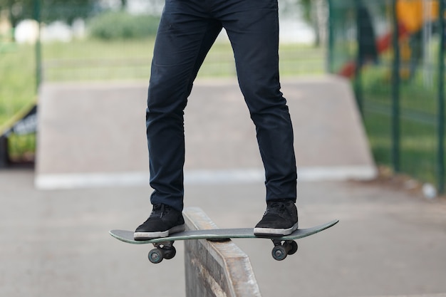 Legs of unknown young guy in black jeans and sneakers on skateboard while performing complicated trick in summer sunny park