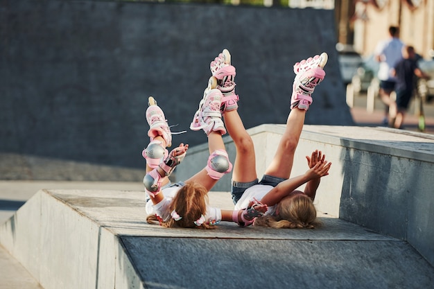 Ноги вверх. Чувствуя себя свободно. На пандусе для экстремальных видов спорта. Две маленькие девочки на роликовых коньках на открытом воздухе весело проводят время.