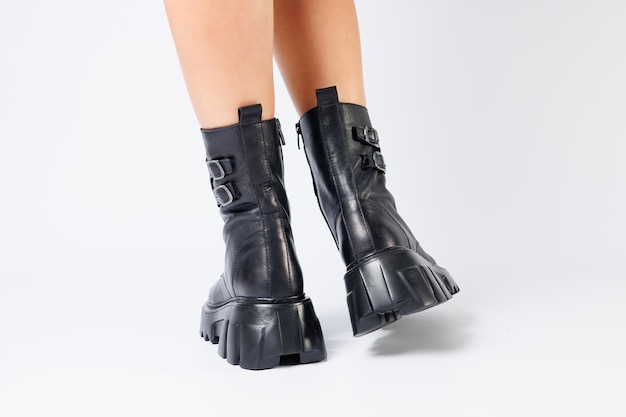 Legs of a woman in black leather boots from a new collection on a white background legs of a girl in fashionable leather boots spring 2022