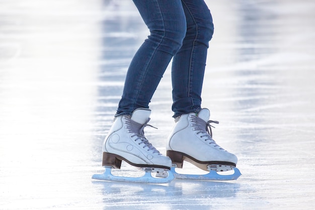 Legs of a woman in blue jeans and white skates on an ice rink. hobbies and leisure.