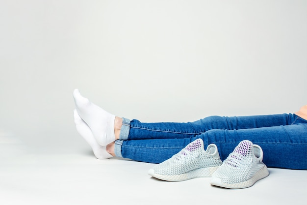 Legs of a woman sitting on the floor on a light background with sneakers 