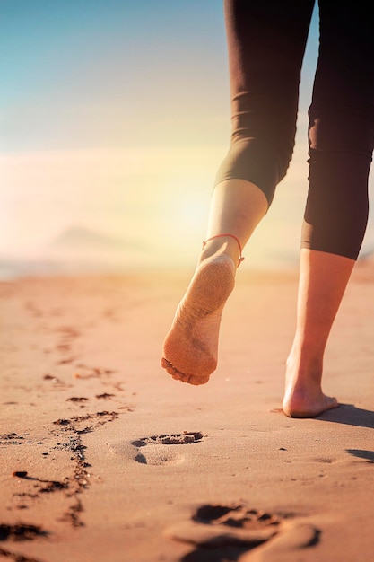 그녀가 걸어갈 때 그녀의 발자국을 표시하는 해변의 모래 위를 걷는 여성의 다리