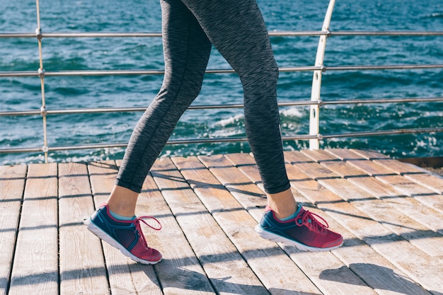 Legs of a young athletic woman in sneakers against the background of the sea