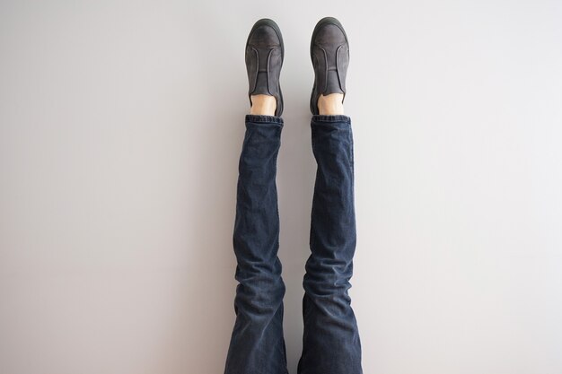 Legs of a young man in jeans and shoes on gray background.