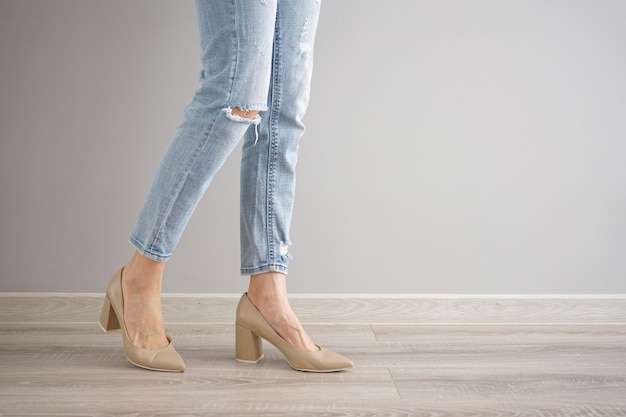 Legs of a young woman in jeans and shoes on gray background, space for text.