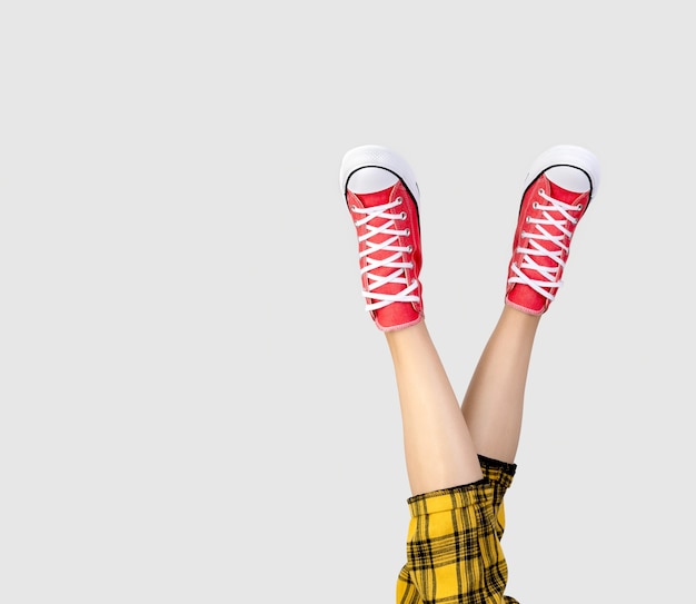 Legs of a young woman in stylish red sneakers on gray background