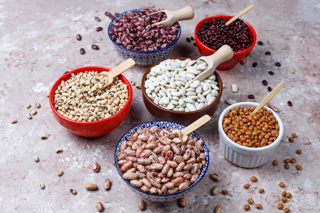 Legumes and beans assortment in different bowls on light stone background . Top view. Healthy vegan protein food.