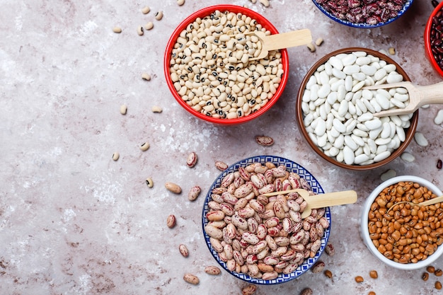 Assortimento di legumi e fagioli in diverse ciotole su fondo in pietra chiara. vista dall'alto. alimento proteico vegano sano.