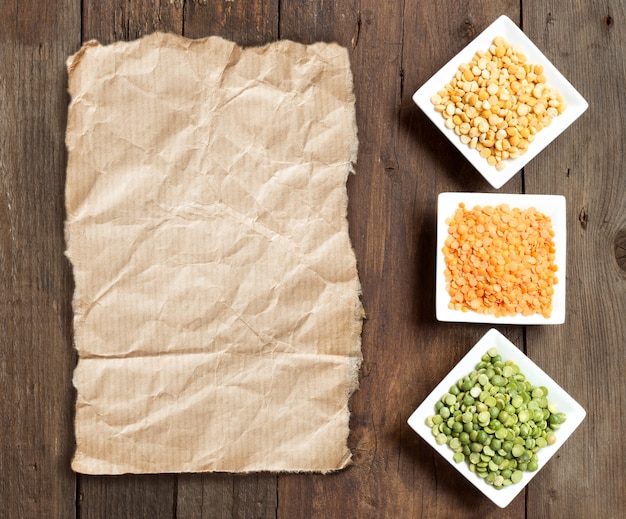 Legumes in bowls on a wooden table top view with paper