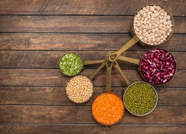 Legumes set in vintage copper scoops on wooden background with copyspace