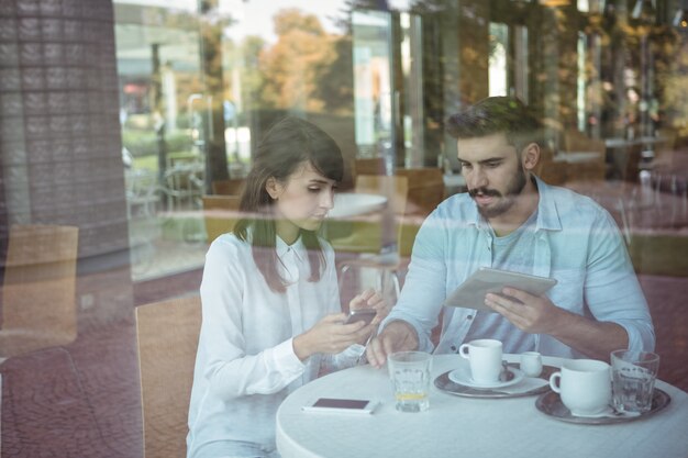 Leidinggevenden met behulp van mobiele telefoon en digitale tablet in cafetaria