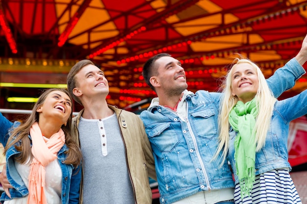 leisure, amusement park and friendship concept - group of smiling friends with carousel on the back