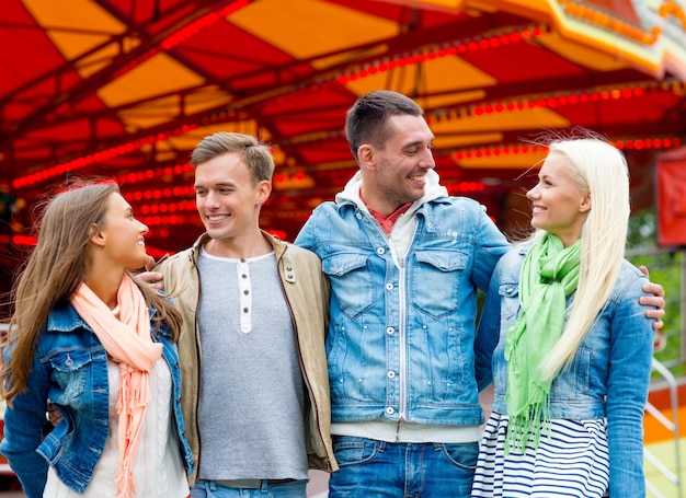 leisure, amusement park and friendship concept - group of smiling friends with carousel on the back