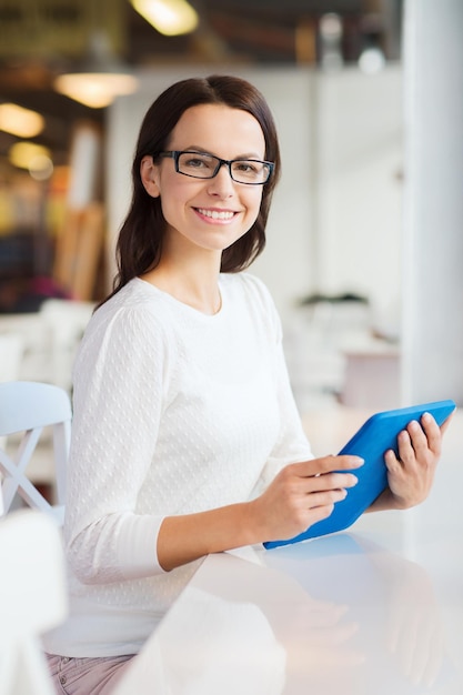 leisure, business, people, technology and lifestyle concept - smiling young woman in eyeglasses with tablet pc computer at cafe