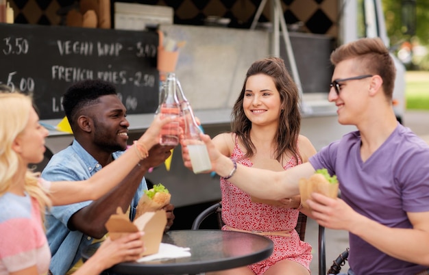 Photo leisure celebration and people concept happy friends clinking bottles of nonalcoholic drinks and eating at food truck