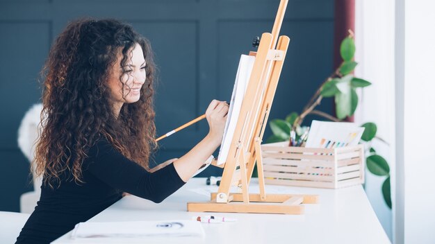 leisure and creation. talented lady with curly hair enjoying painting at home studio