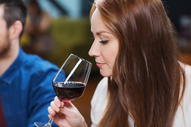 Фото Концепция отдыха, напитков, дегустации, людей и праздников - улыбающаяся женщина пьет красное вино в ресторане