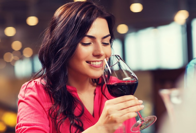 Foto tempo libero, bevande, degustazione, persone e vacanze concetto - donna sorridente che beve vino rosso al ristorante