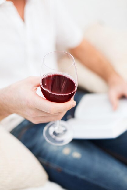 leisure, drinks, education and lifestyle concept - close up of male hand holdind book and glass of red wine