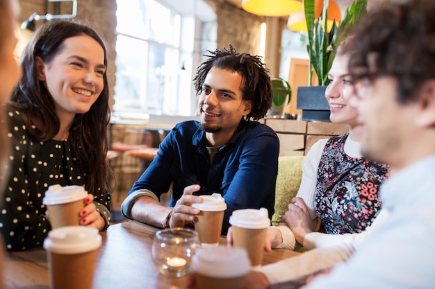 leisure, drinks, people and communication concept - happy friends drinking coffee from disposable paper cups at restaurant or cafe