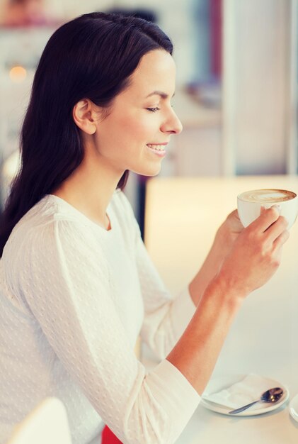 レジャー、飲み物、人々、ライフスタイルのコンセプト-カフェでコーヒーを飲む若い女性の笑顔