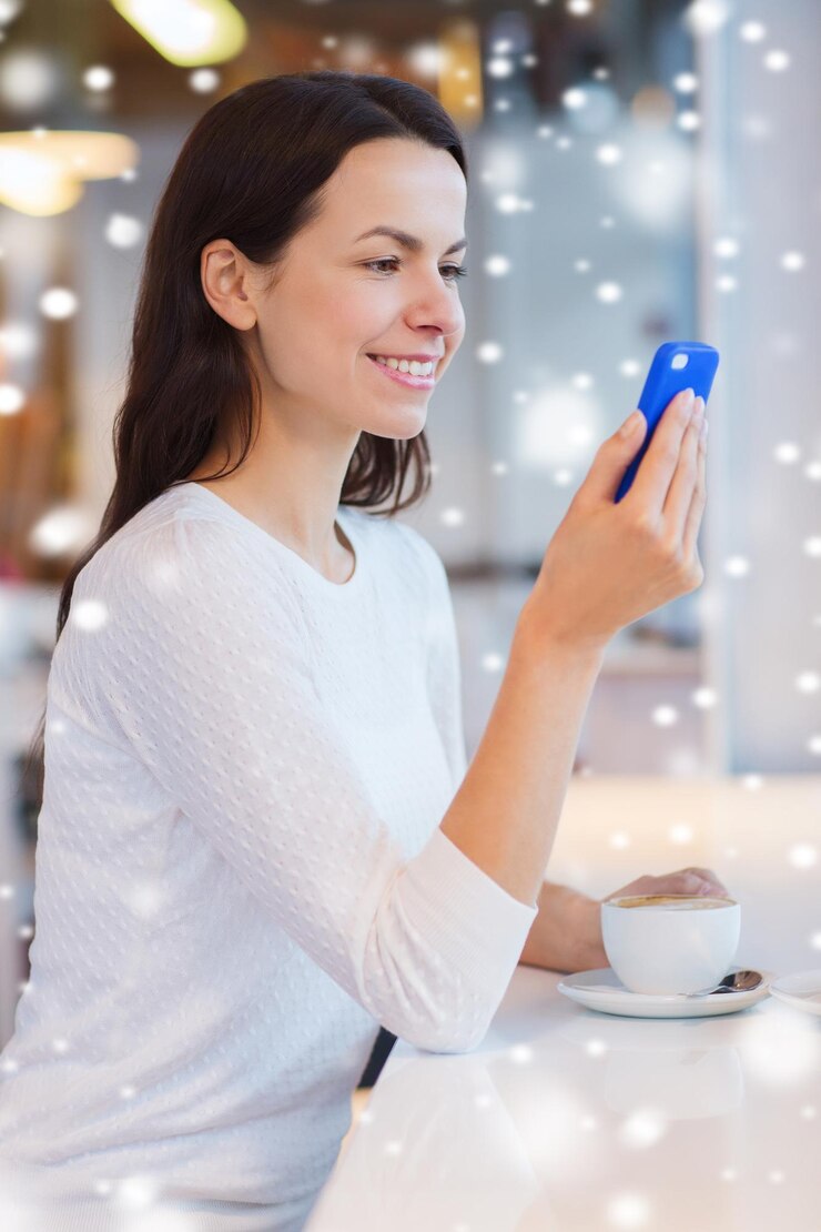 Photo leisure, drinks, people, technology and lifestyle concept - smiling young woman with smartphone drinking coffee at cafe with snow effect