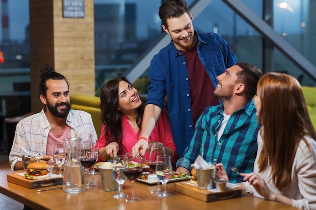 leisure, eating, food and drinks, people and holidays concept - smiling friends having dinner and drinking red wine at restaurant