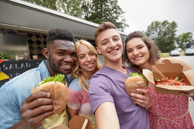 Foto cibo per il tempo libero e concetto di persone amici felici con wok e hamburger che si fanno selfie al food truck