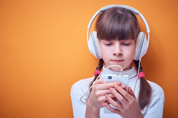 Leisure and entertainment , Caucasian teen girl listening to music with headphones using the phone on a colored