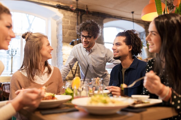 leisure, food, drinks, people and holidays concept - happy friends eating and drinking at restaurant