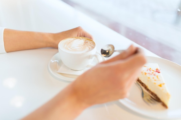 レジャー、食べ物、飲み物、人々、ライフスタイルのコンセプト – カフェでケーキを食べ、コーヒーを飲む若い女性の手の接写