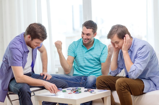 Photo leisure, games and lifestyle concept - happy three male friends playing poker at home