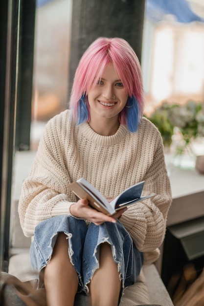 Leisure A girl with pink hair reading a book near the window